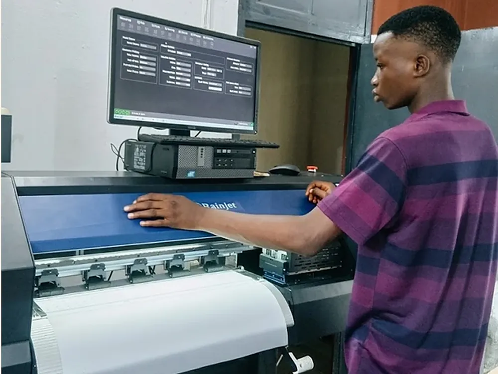 A machinist setting up a job at the DTF printer, the print software open on the screen behind